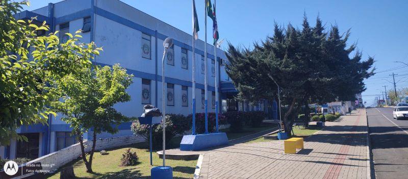 Fachada do Paço Municipal de Pinhão, com árvores, mastros de bandeiras e calçada em frente ao prédio da Prefeitura.